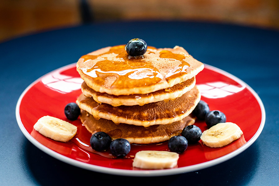 Stack of pancakes with syrup and fresh fruit on bright red plate.