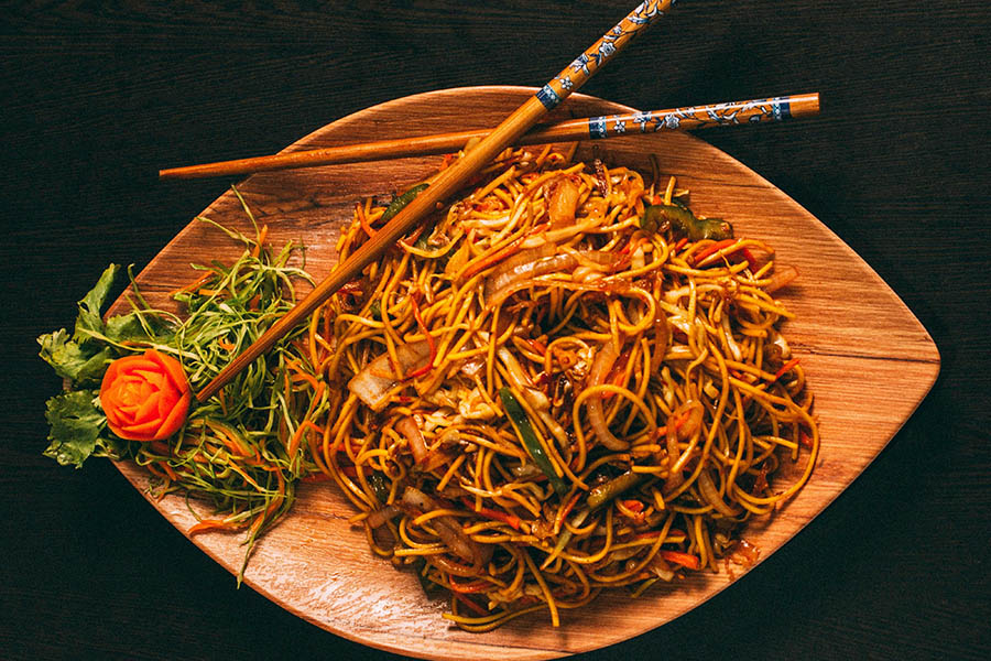 Oval wood plate with pile of Chinese noodles and chop sticks.